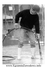Pracownik przedstawiony na zdjęciu zagęszcza mieszankę betonową przy 